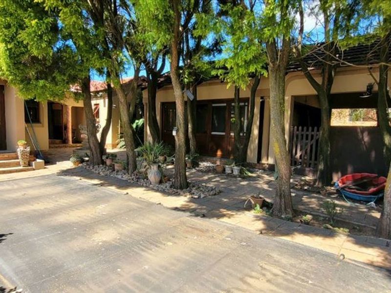 A shaded outdoor pool area featuring a paved patio, mature trees, and direct access to the main residence through timber-framed doors.