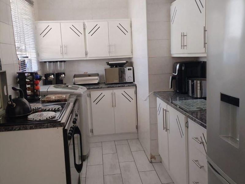 A functional kitchen featuring white cabinetry, tiled flooring, and tiled wall finishes, offering a clean but dated aesthetic ready for modernization.