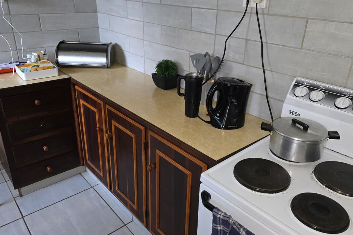 A functional kitchen area featuring dark wood-toned cabinetry, a light-colored laminate countertop, and a white freestanding electric stove with a tiled backsplash.