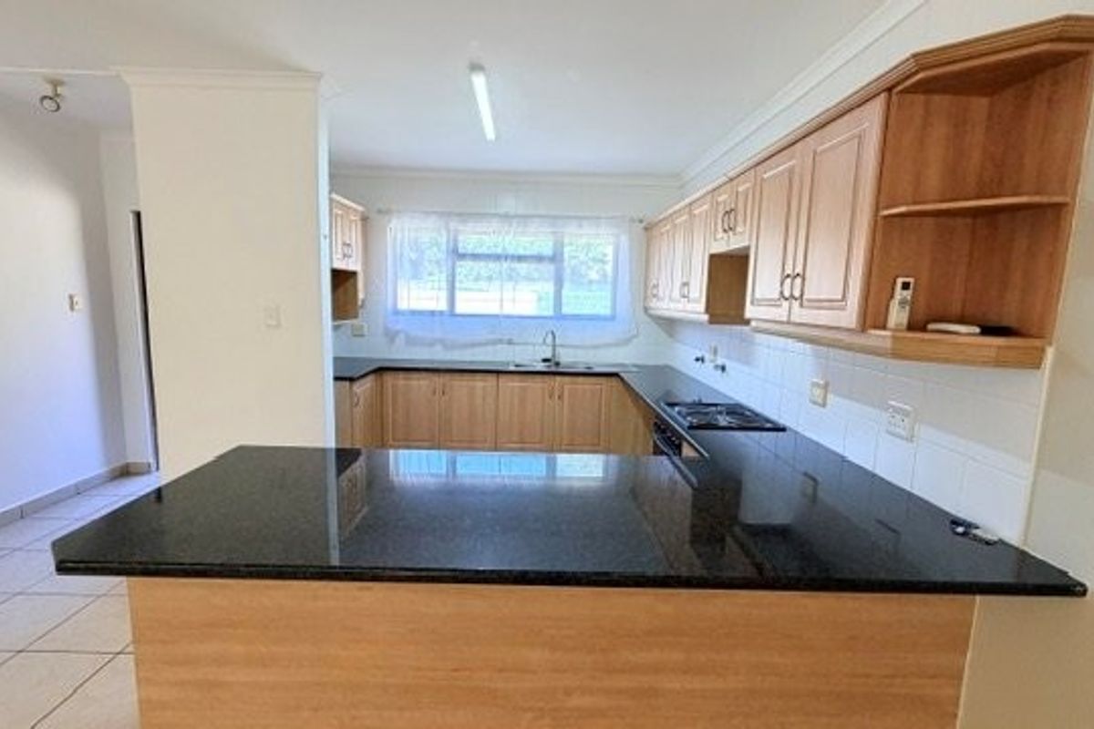 A functional kitchen featuring wooden cabinetry, granite countertops, a built-in hob and oven, and tiled flooring, offering a clean and practical workspace.
