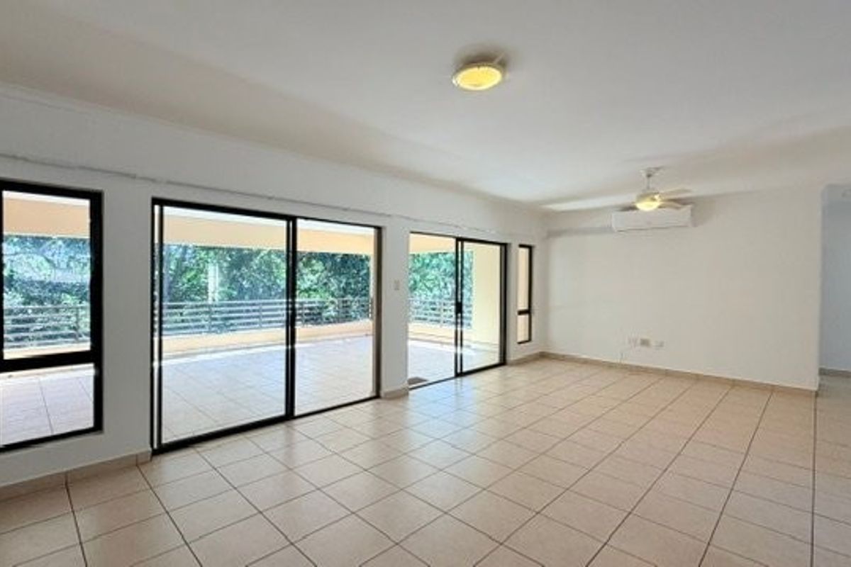 Spacious, light-filled living area featuring neutral tiled flooring, split-system air conditioning, and large sliding glass doors opening onto a private balcony.