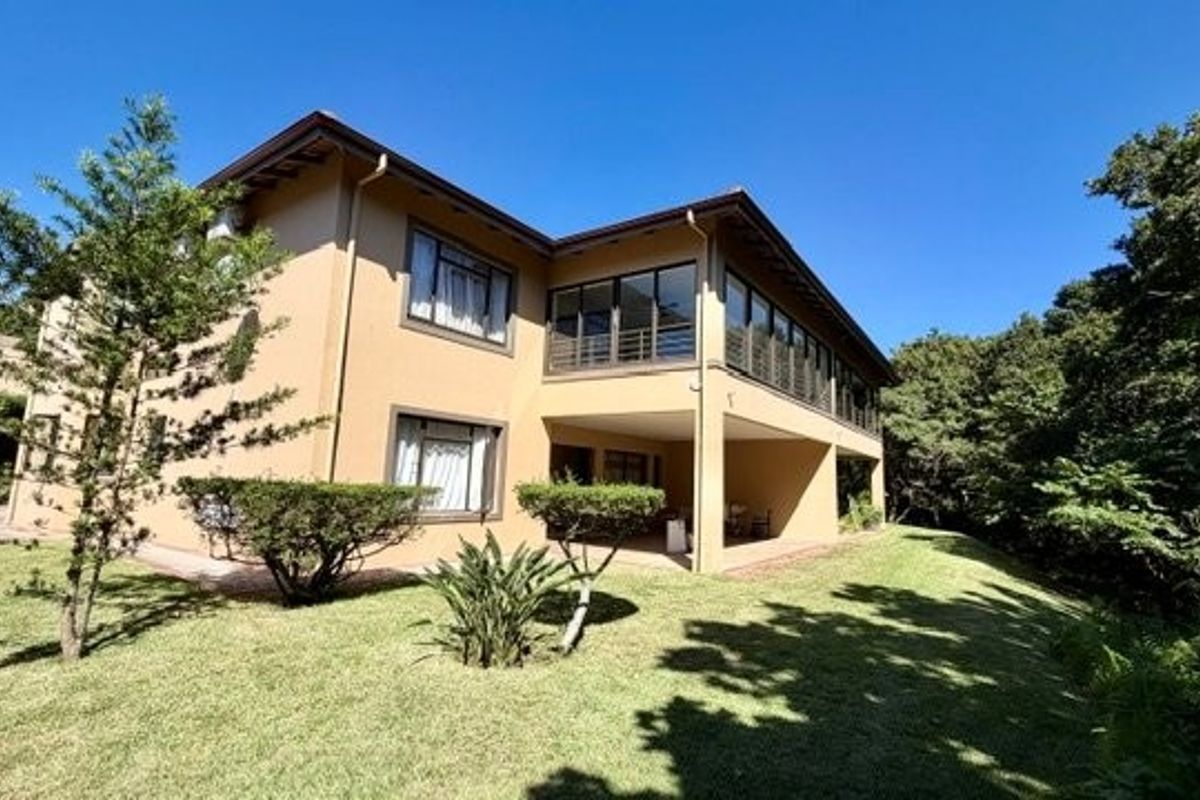 Rear view of the apartment building featuring a covered patio, balcony, and well-maintained garden area.