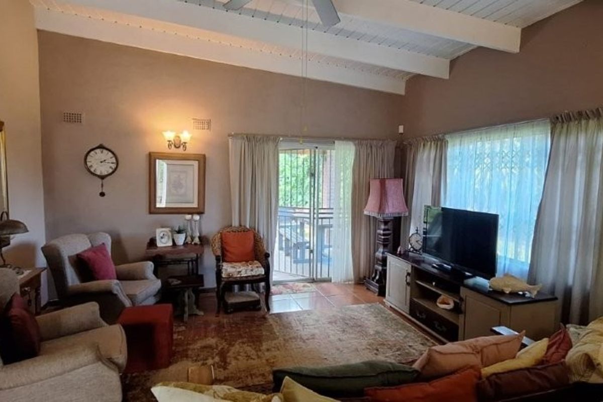 Spacious living room featuring a vaulted ceiling with exposed beams, ceiling fan, and direct access to an outdoor patio area through sliding glass doors.