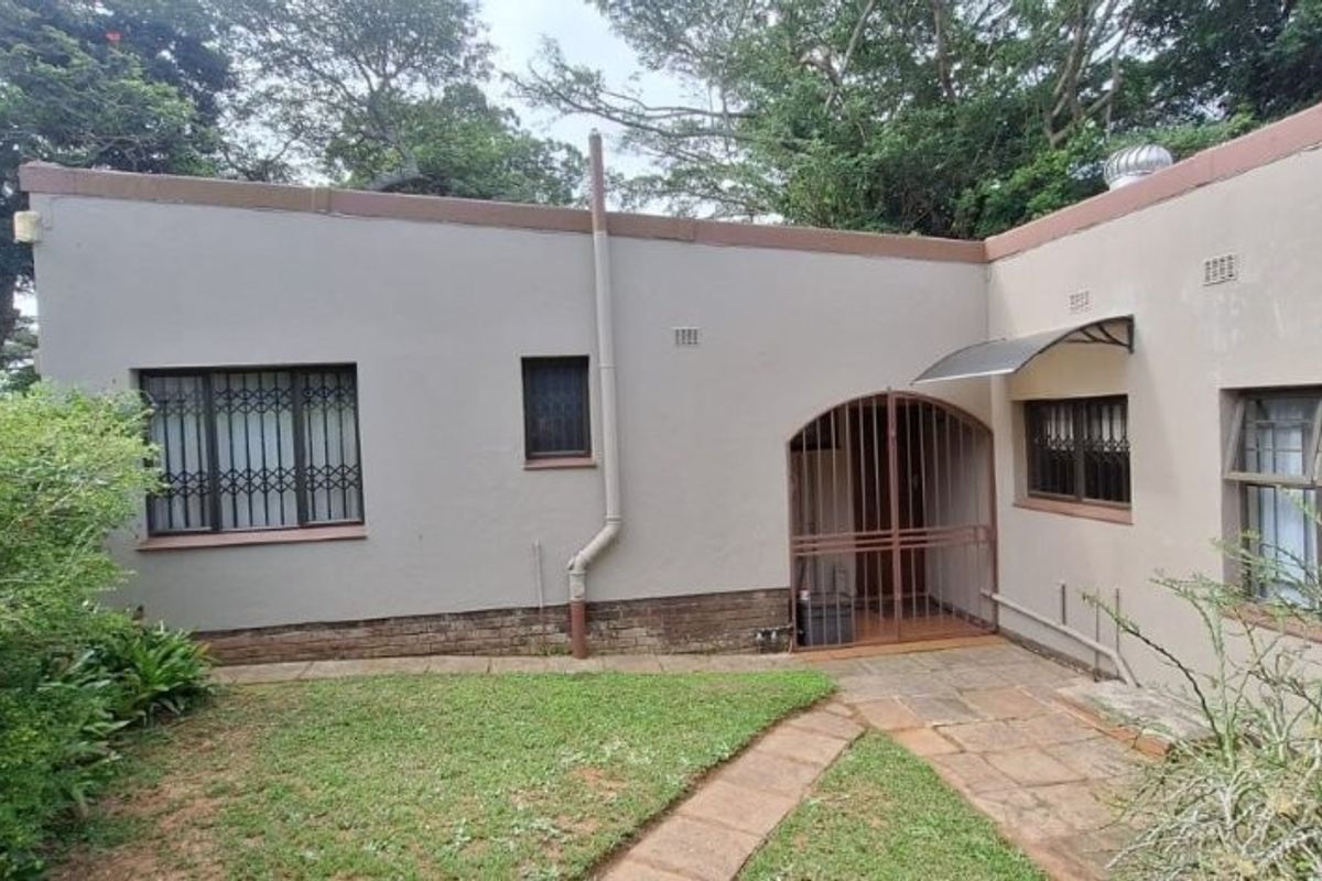 Rear exterior view of the townhouse featuring a small garden, paved walkway, security gates, and security bars on the windows.