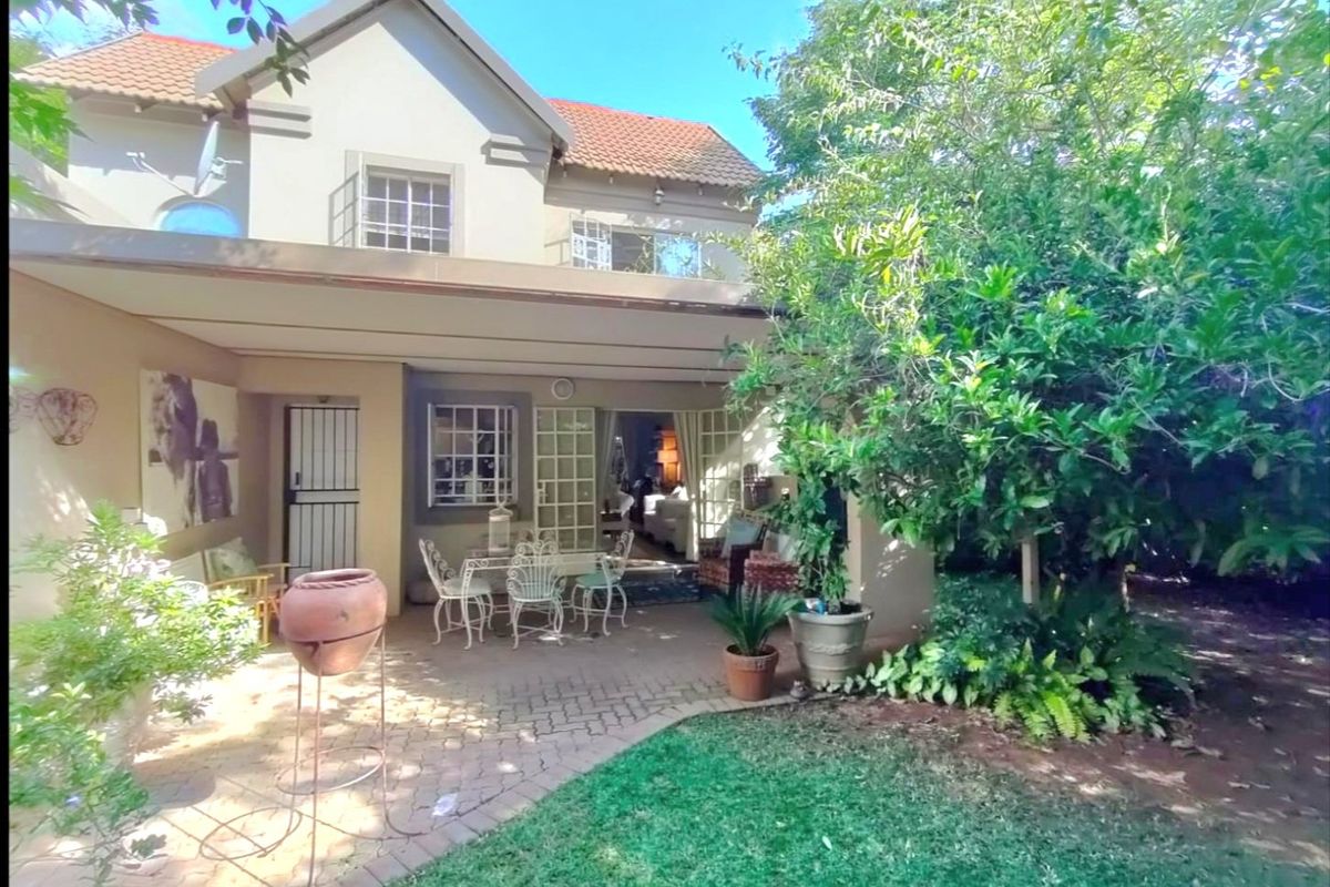 Rear view of the townhouse featuring a covered patio, paved outdoor area, and established garden, providing a private space for outdoor relaxation.