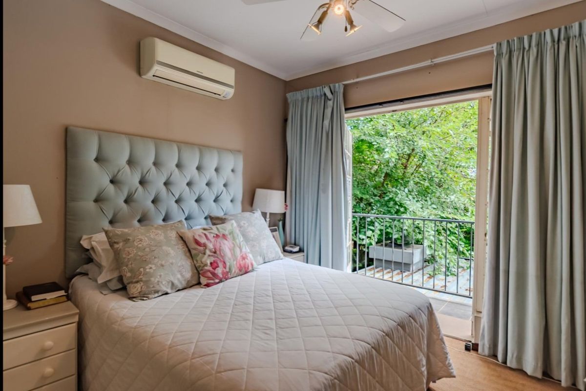A comfortable bedroom featuring a split-system air conditioner, ceiling fan, and direct access to a private balcony through sliding glass doors.