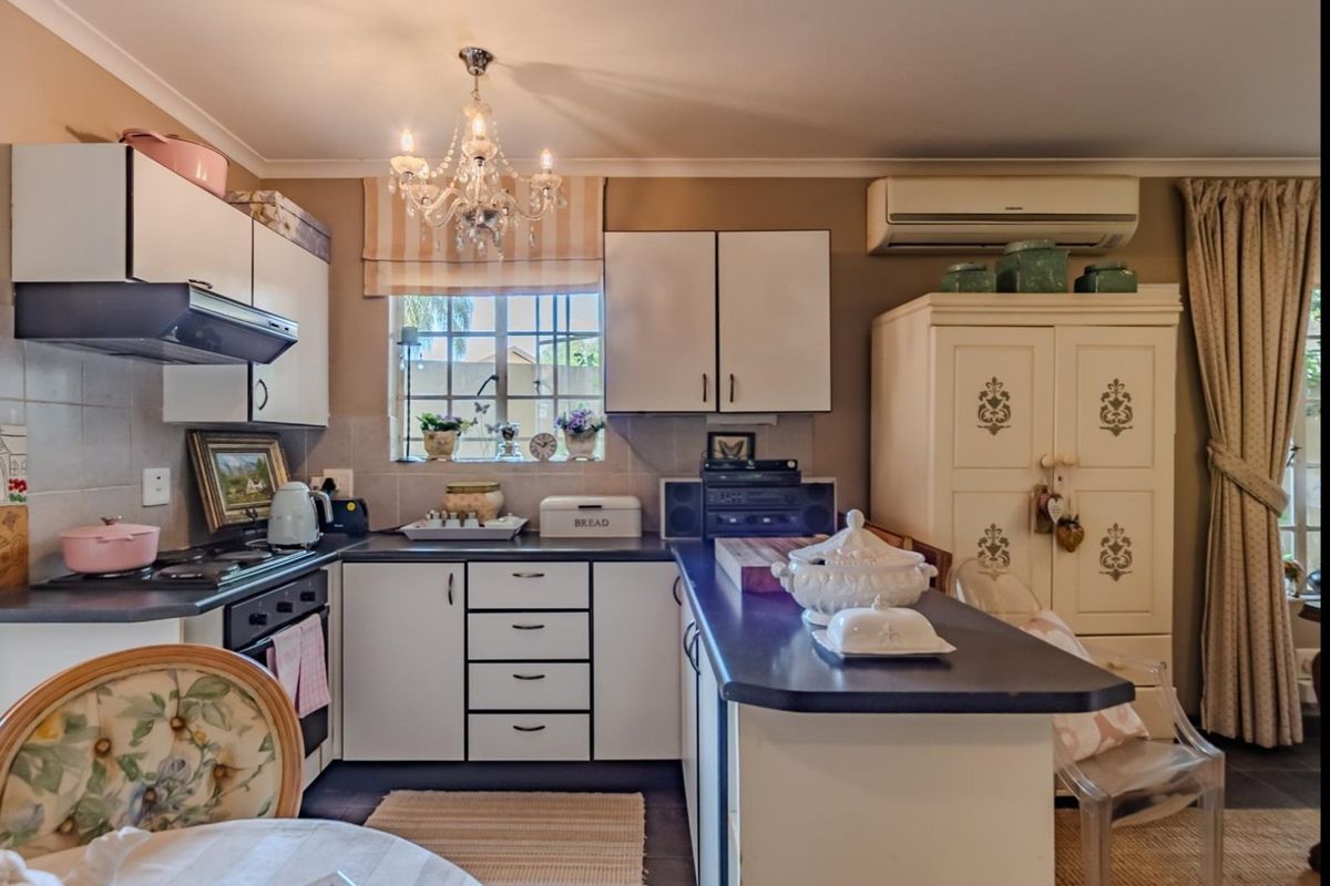 A functional kitchen featuring white cabinetry, dark laminate countertops, built-in oven and hob, and a wall-mounted air conditioning unit.
