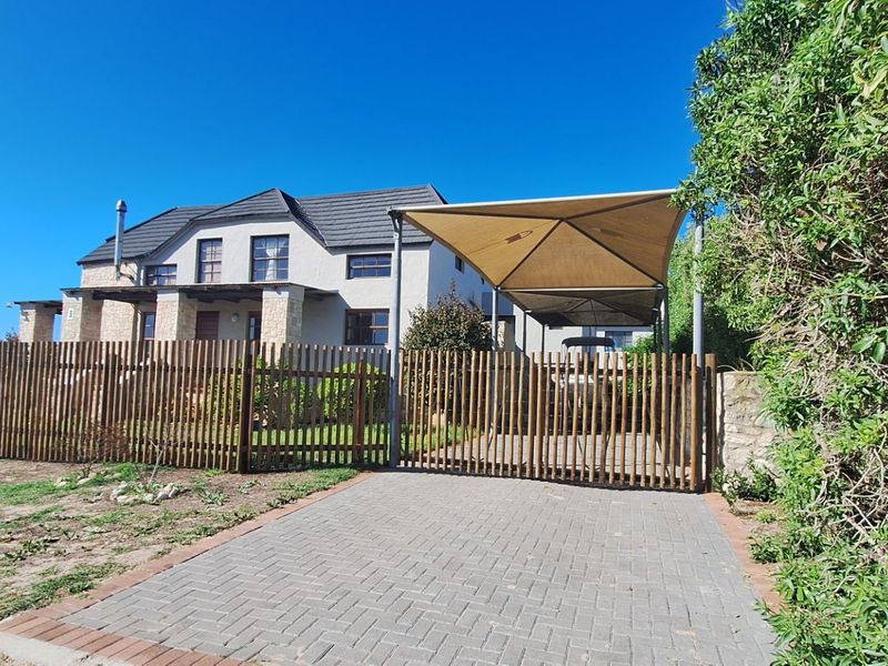 Front view of a two-story house featuring stone cladding, a tiled roof, a paved driveway, and a shaded carport behind a timber fence.
