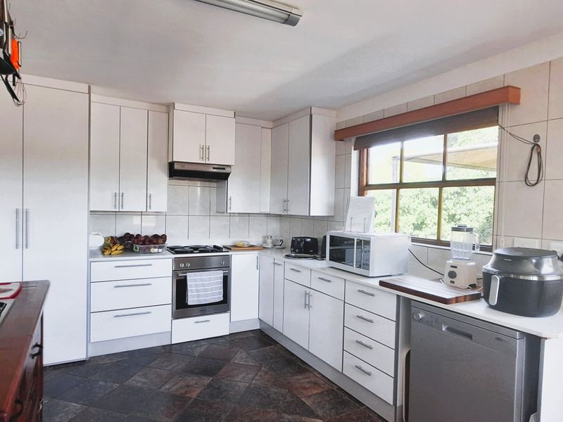 A functional kitchen featuring white cabinetry, stone countertops, a gas hob, and tiled flooring, offering a clean and practical workspace.