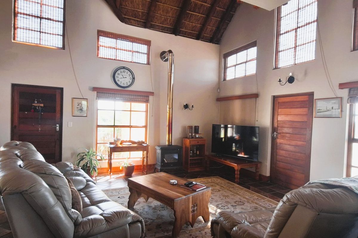Spacious living room featuring a high vaulted thatched ceiling with exposed rafters, a central wood-burning fireplace, and large windows providing ample natural light.