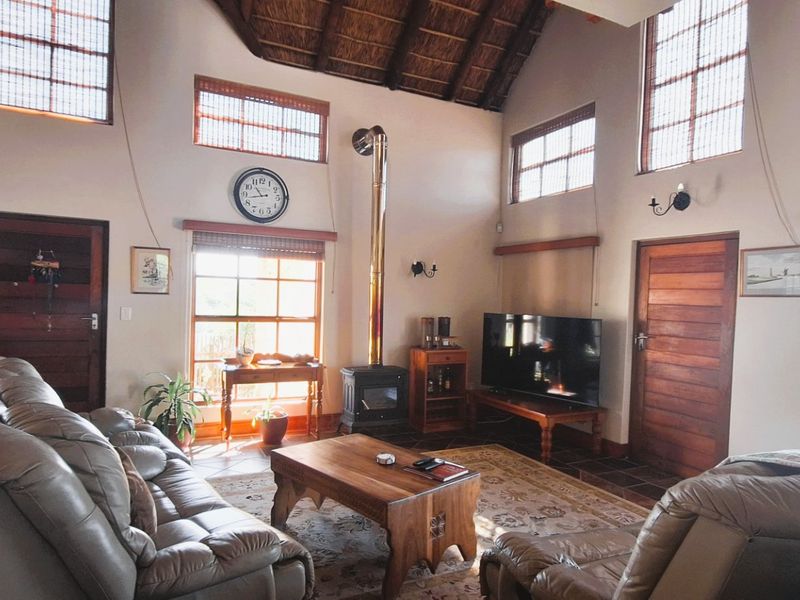 Spacious living room featuring a high vaulted thatched ceiling with exposed rafters, a central wood-burning fireplace, and large windows providing ample natural light.