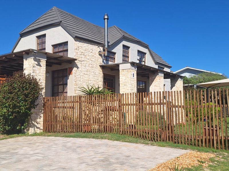 A well-maintained house featuring stone cladding, a tiled roof, a timber pergola, and a paved driveway, enclosed by a timber picket fence.