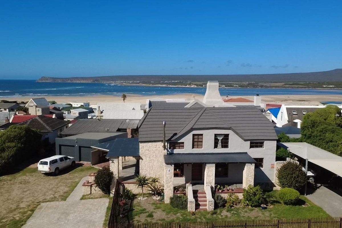 Aerial view of a coastal residence featuring stone cladding, a tiled roof, and a covered porch, situated near the beach.