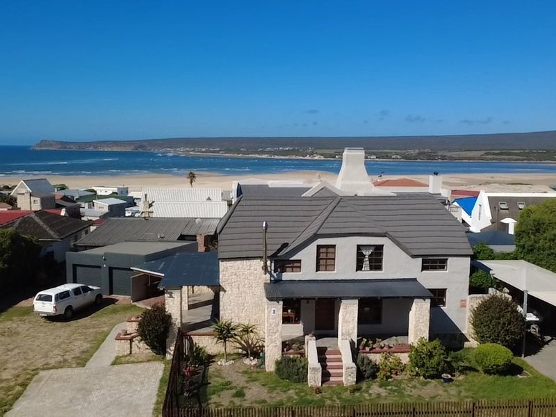 Aerial view of a coastal residence featuring stone cladding, a tiled roof, and a covered porch, situated near the beach.