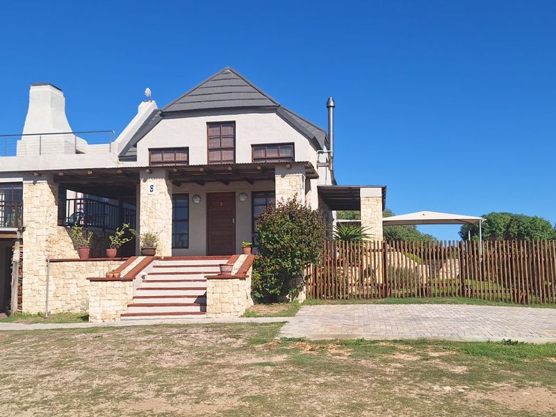 A charming stone-clad house featuring a timber pergola, front entrance steps, and a paved driveway, set within a well-maintained garden area.