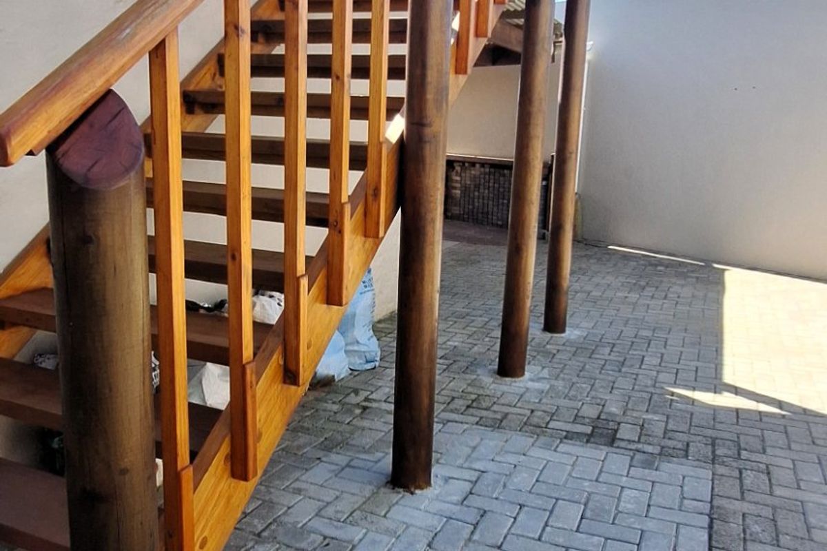 An exterior rear courtyard featuring a wooden staircase leading to an upper level, set against a paved area and boundary wall.