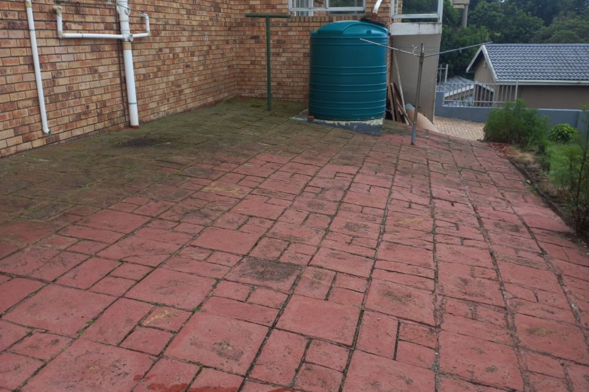 Rear exterior area featuring a paved patio, brick facade, and a water storage tank, requiring maintenance and cleaning to improve the outdoor space.