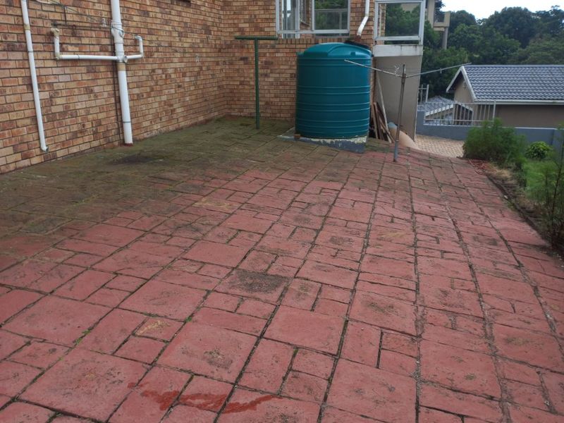 Rear exterior area featuring a paved patio, brick facade, and a water storage tank, requiring maintenance and cleaning to improve the outdoor space.