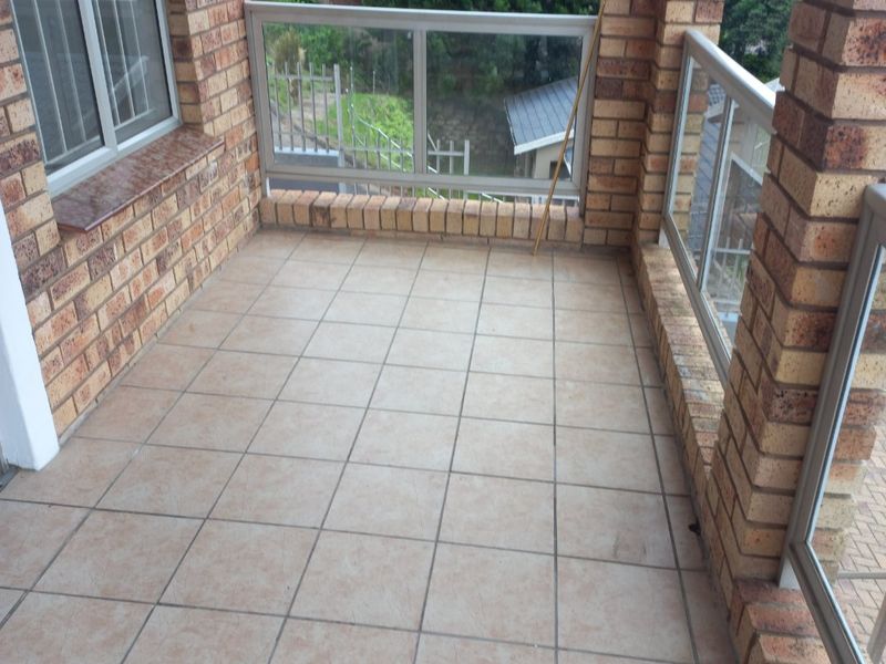 A covered balcony featuring face brick pillars, tiled flooring, and a glass balustrade, offering an open outdoor space.