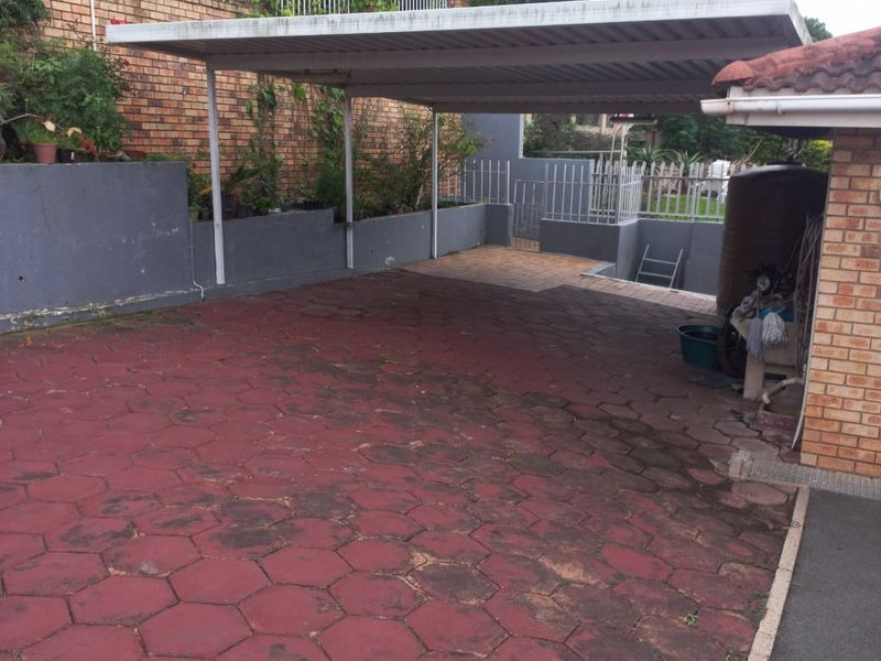 A paved driveway area featuring a covered carport, brick retaining walls, and perimeter fencing, providing functional off-street parking space.