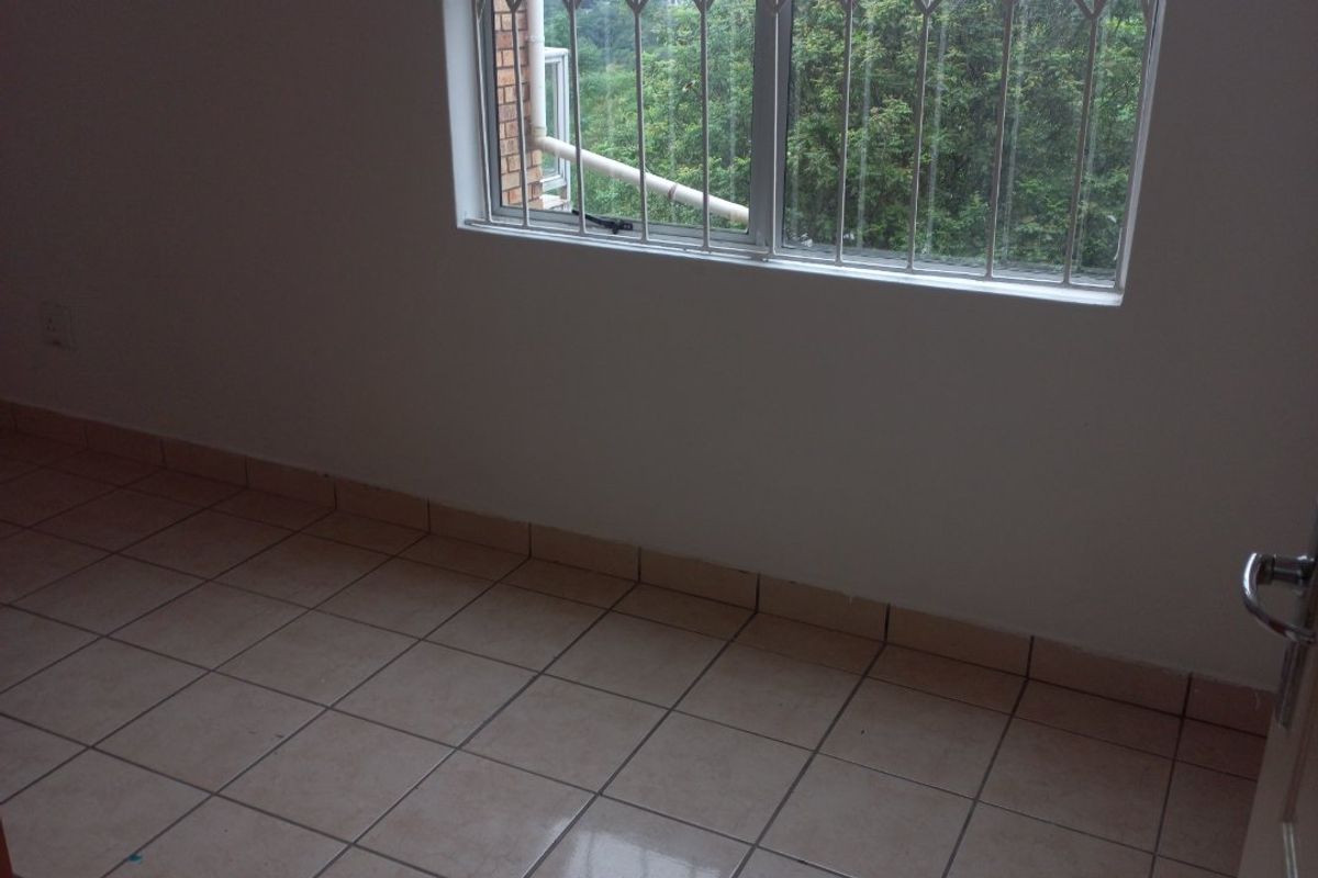 An empty bedroom featuring tiled flooring and a window fitted with a security gate.