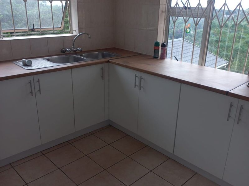 A functional kitchen featuring white cabinetry, laminate countertops, a double bowl sink, and tiled flooring with security bars on the windows.