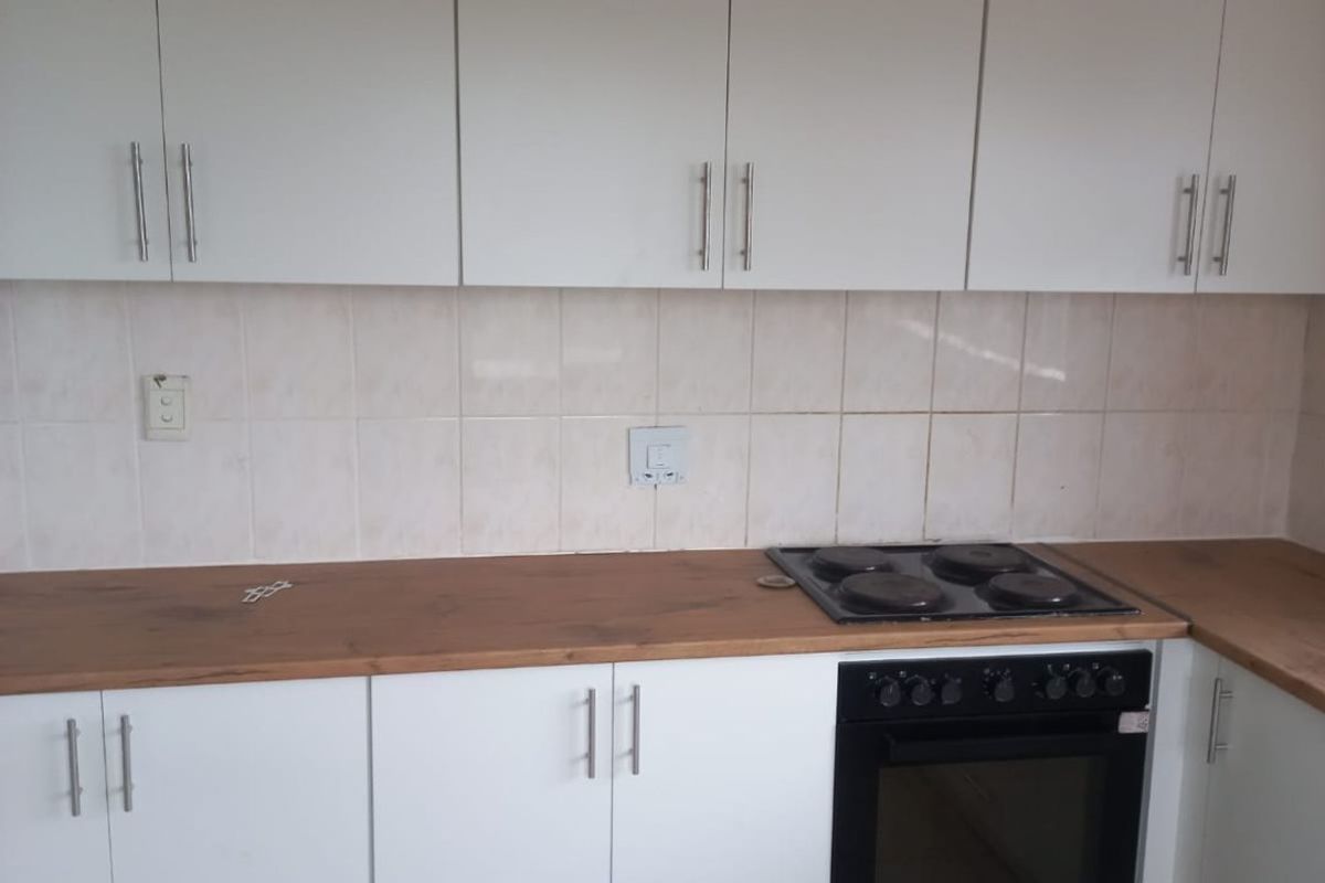 A functional kitchen featuring white cabinetry, wood-look countertops, a built-in oven, and an electric hob with tiled splashbacks and flooring.