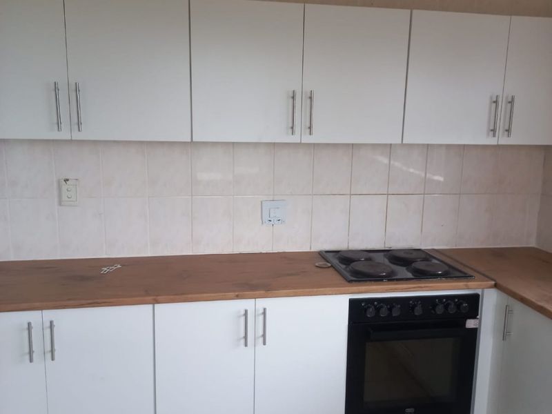 A functional kitchen featuring white cabinetry, wood-look countertops, a built-in oven, and an electric hob with tiled splashbacks and flooring.