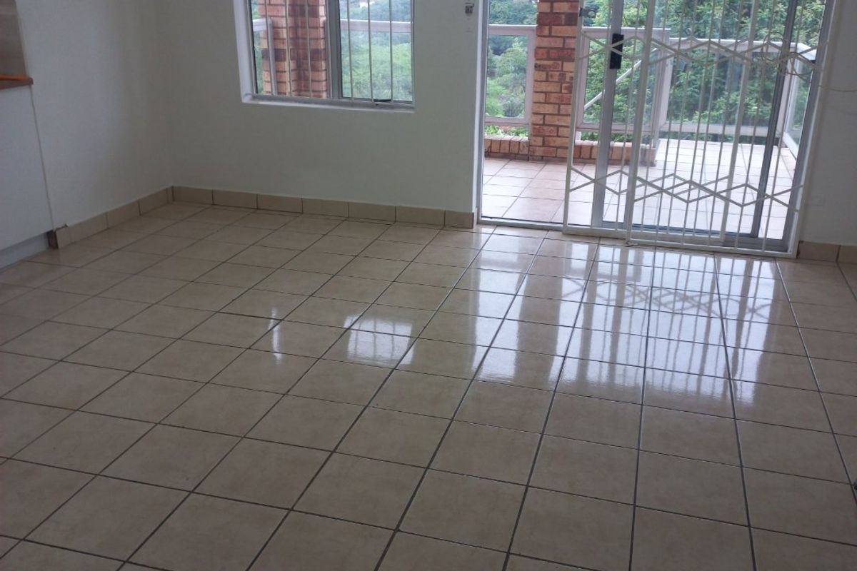 An empty living area featuring ceramic floor tiles, large windows with burglar bars, and a sliding glass door leading to an outdoor patio.