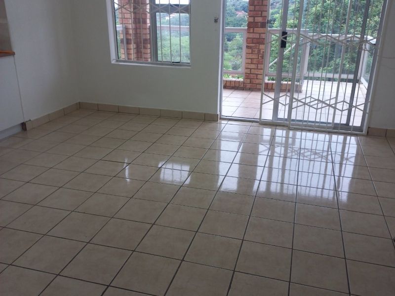 An empty living area featuring ceramic floor tiles, large windows with burglar bars, and a sliding glass door leading to an outdoor patio.