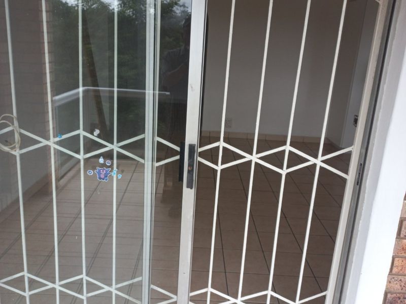 A covered balcony area featuring tiled flooring, a sliding glass door, and a fitted security gate.