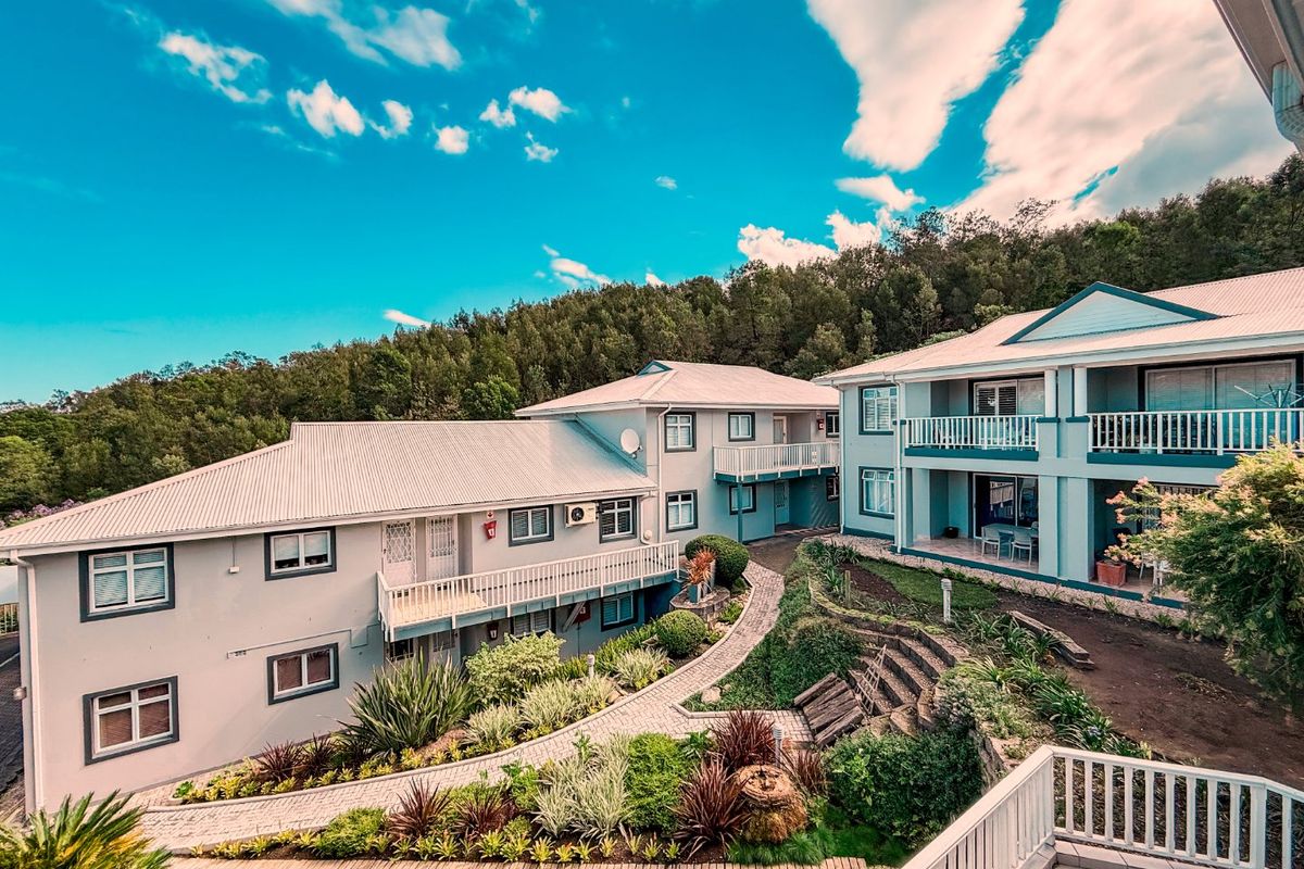An elevated view of a multi-level apartment complex featuring landscaped gardens, paved walkways, and private balconies with white railings.