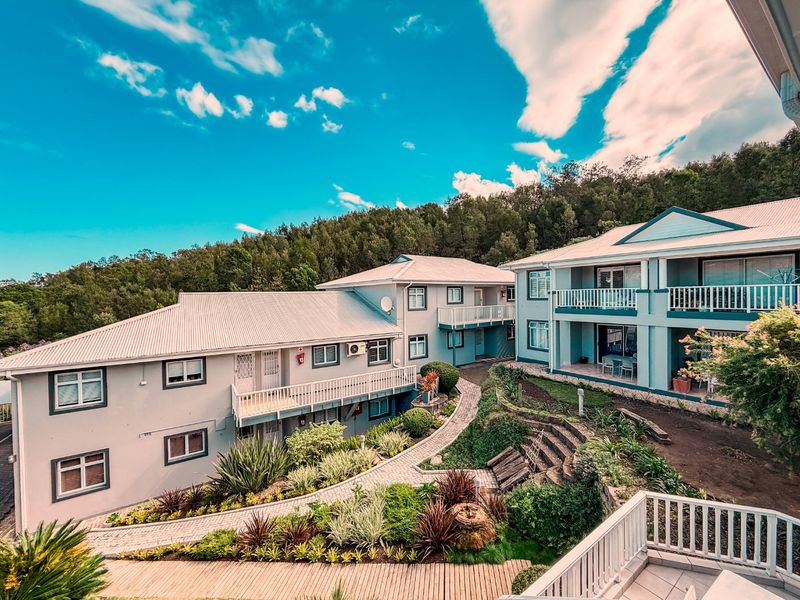 An elevated view of a multi-level apartment complex featuring landscaped gardens, paved walkways, and private balconies with white railings.