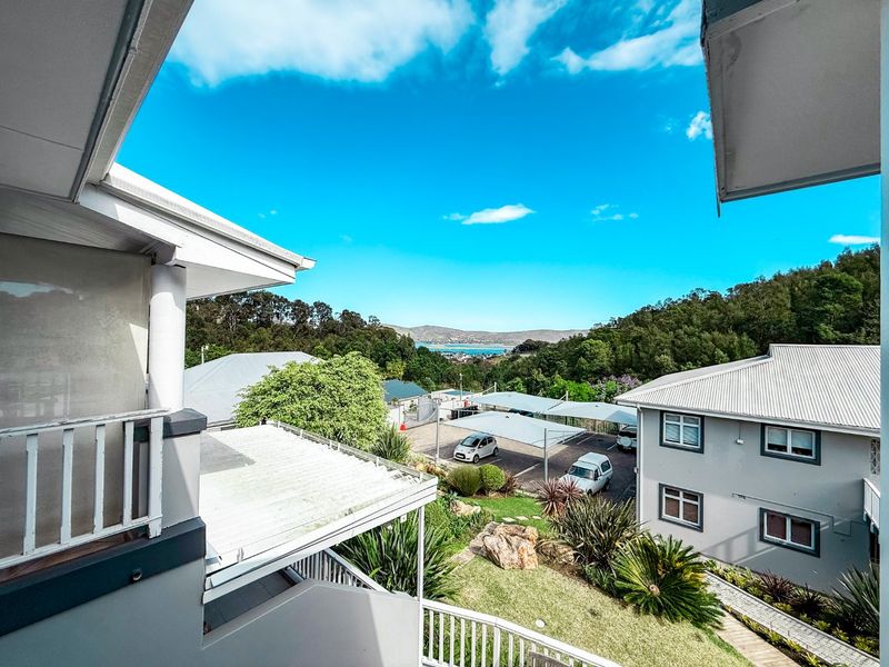 Elevated view overlooking the apartment complex grounds, parking area with shade ports, and distant coastal landscape.