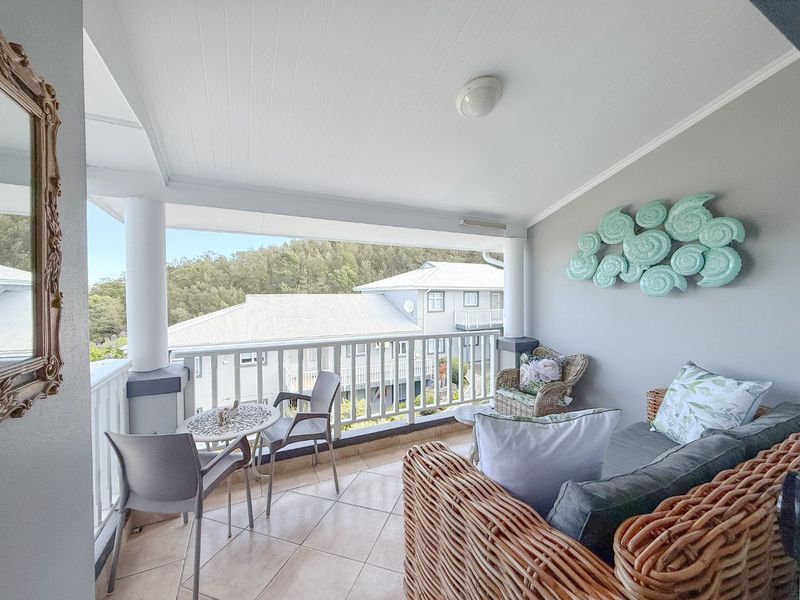 A covered balcony featuring tiled flooring, white railings, and support columns, offering an elevated view of the surrounding residential area.