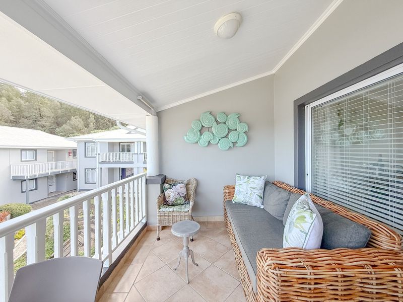 A covered balcony featuring tiled flooring, white railings, and neutral wall finishes, offering a pleasant outdoor space for relaxation.