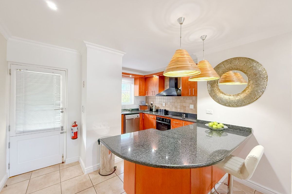 A functional kitchen featuring wooden cabinetry, granite countertops, a breakfast bar, and built-in appliances, with tiled flooring and a neutral color palette.
