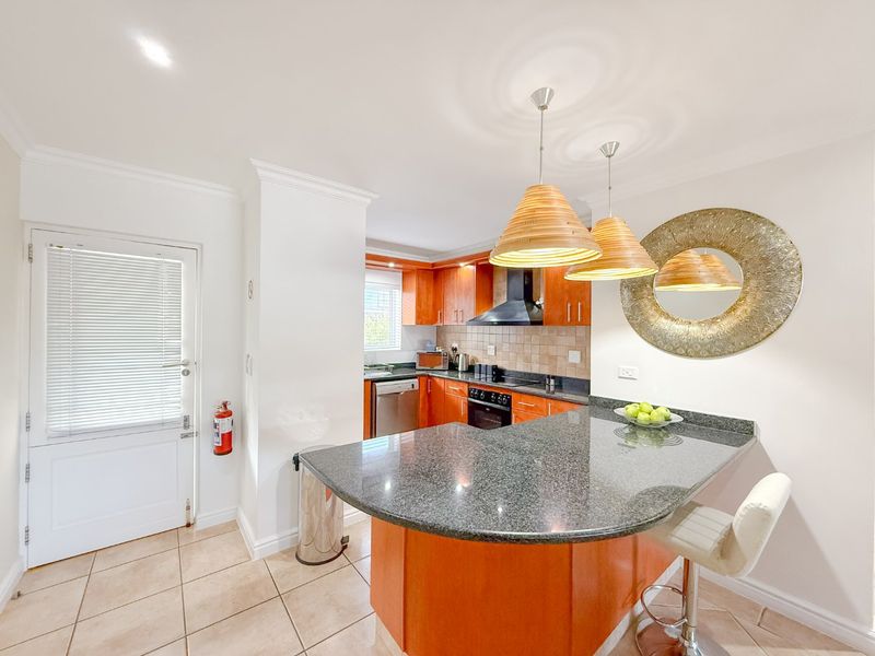 A functional kitchen featuring wooden cabinetry, granite countertops, a breakfast bar, and built-in appliances, with tiled flooring and a neutral color palette.
