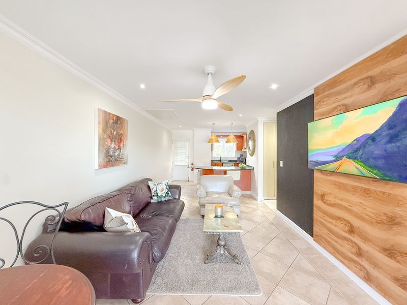 Open-plan living area featuring tiled floors, a wood-accented feature wall, and a connected kitchen with cabinetry, creating a functional and cohesive living space.