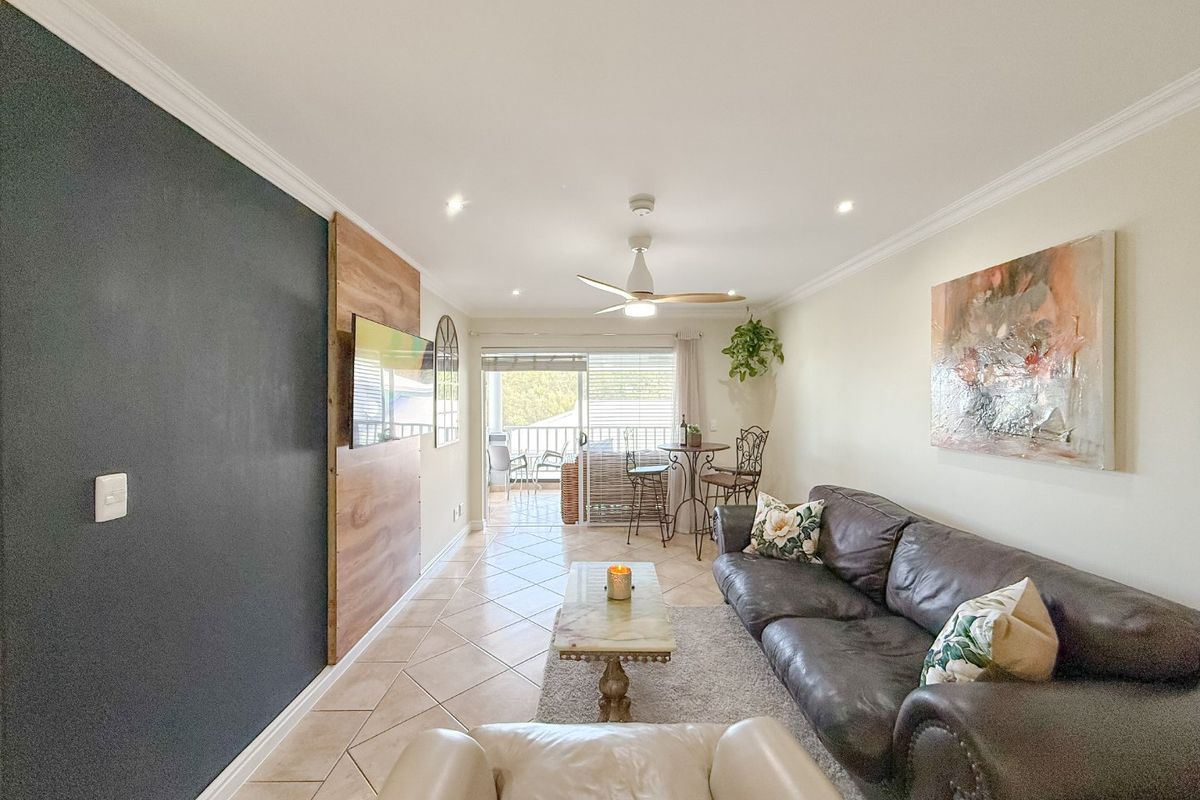 A well-lit living room featuring tiled flooring, a ceiling fan, and an accent wall, with direct access to an outdoor balcony through sliding glass doors.