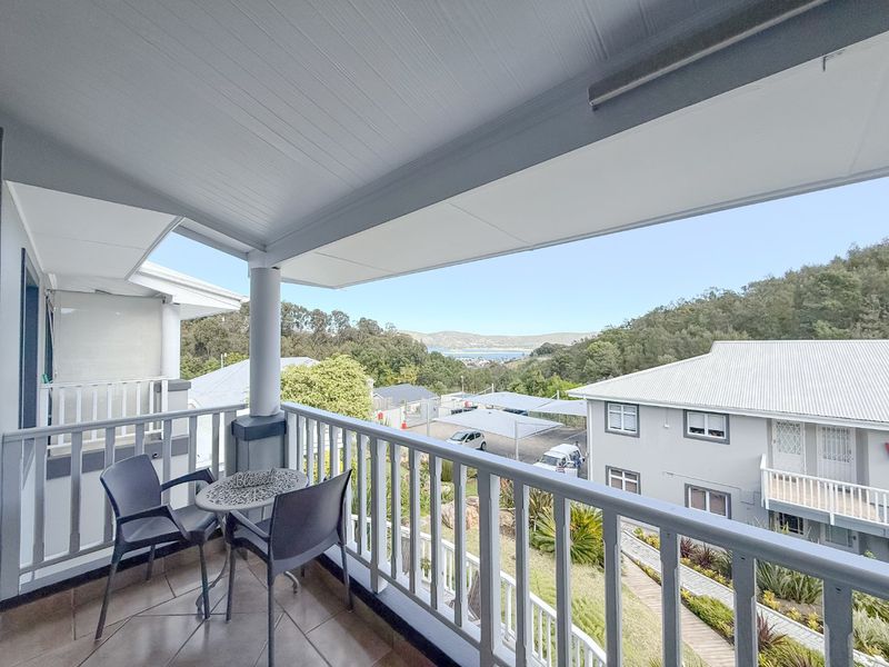 A covered balcony featuring tiled flooring and a railing, offering scenic views of the surrounding landscape and neighborhood.