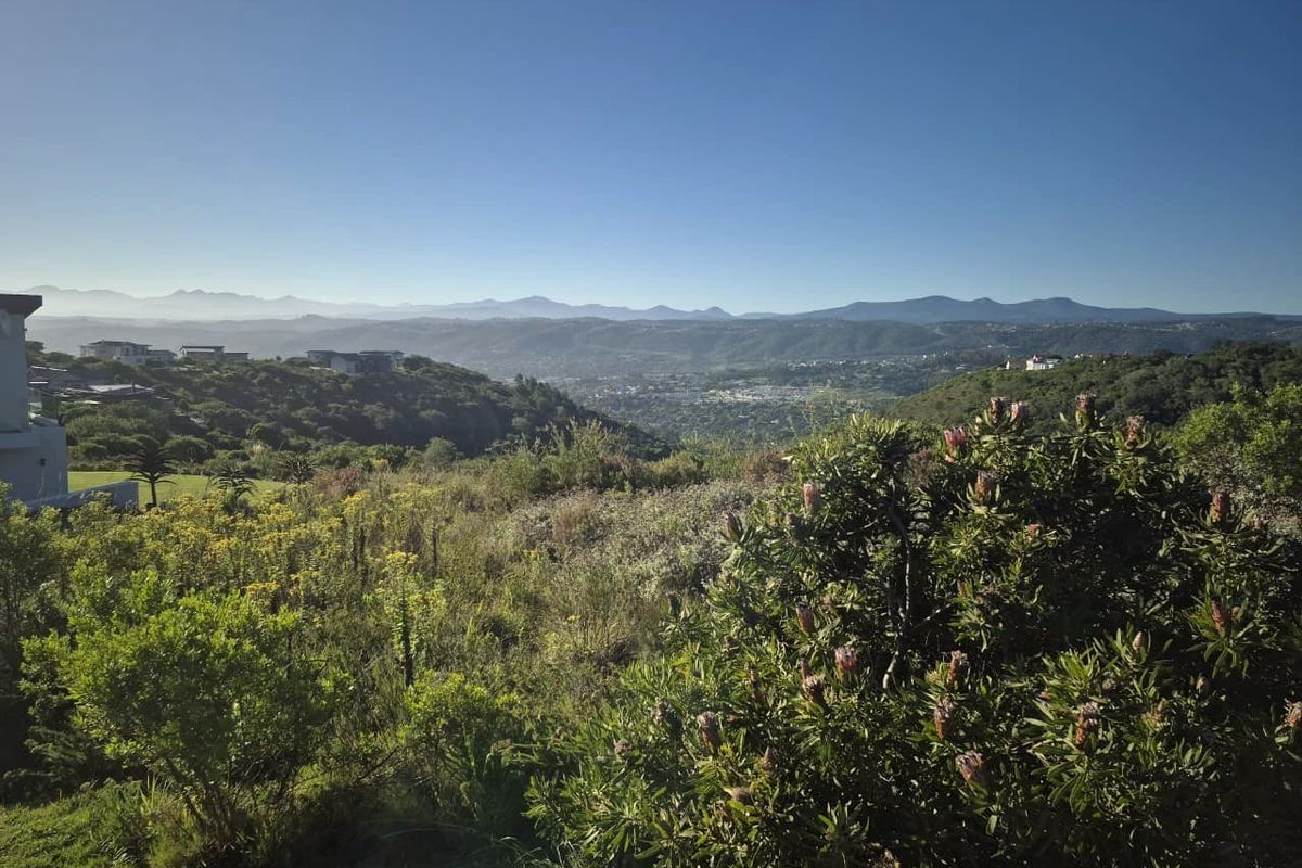 A scenic elevated view overlooking a lush valley with distant mountain ranges, showcasing the natural landscape of the residential land.