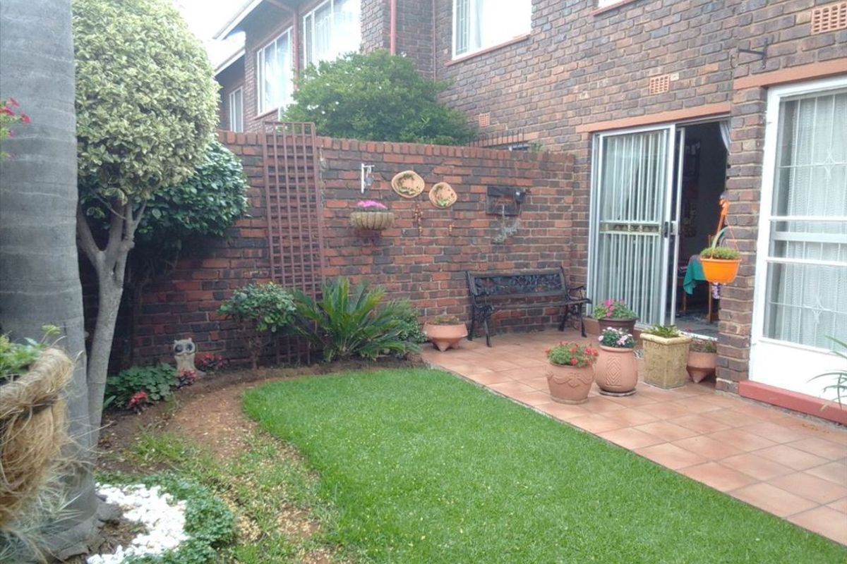 A private rear courtyard featuring a paved patio area, a small lawn, and a brick boundary wall, accessible via sliding glass doors.