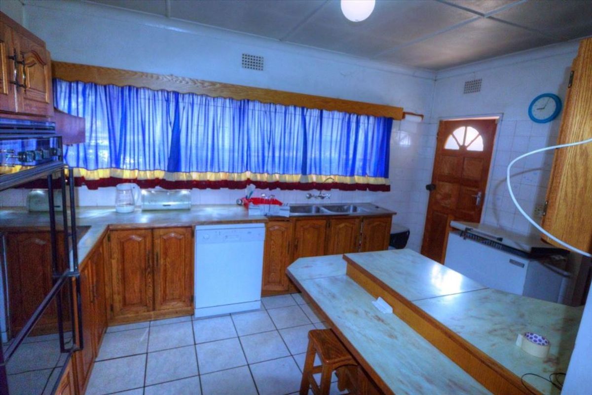A dated kitchen featuring wooden cabinetry, tiled flooring, and a double basin sink, offering significant potential for a modern renovation.