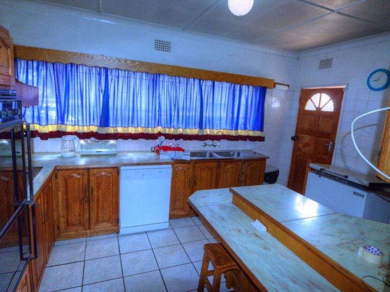 A dated kitchen featuring wooden cabinetry, tiled flooring, and a double basin sink, offering significant potential for a modern renovation.