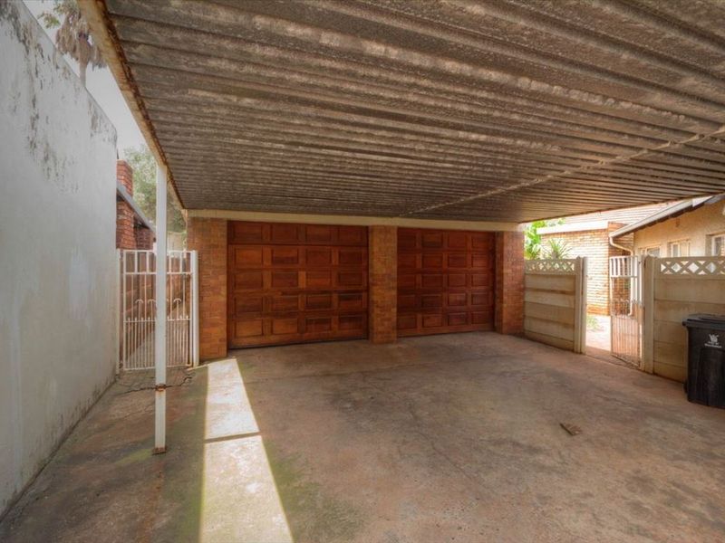 A double garage featuring wooden doors, a corrugated metal roof, and a concrete driveway, enclosed by perimeter walls and security gates.