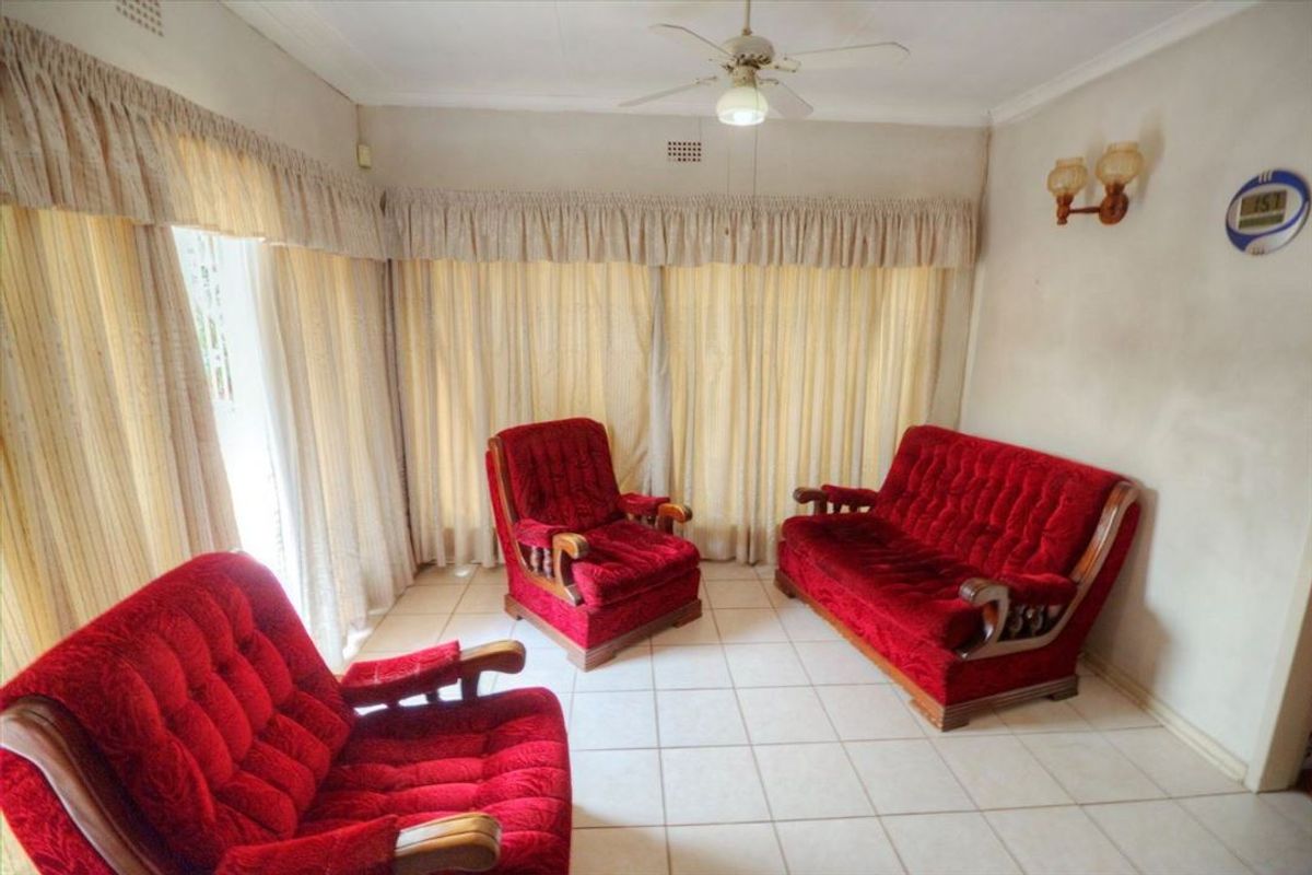 A living room featuring tiled flooring, a ceiling fan, and wall-mounted lighting, with neutral wall finishes and floor-to-ceiling curtains.