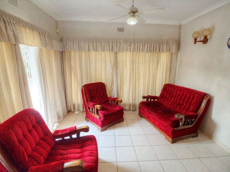 A living room featuring tiled flooring, a ceiling fan, and wall-mounted lighting, with neutral wall finishes and floor-to-ceiling curtains.