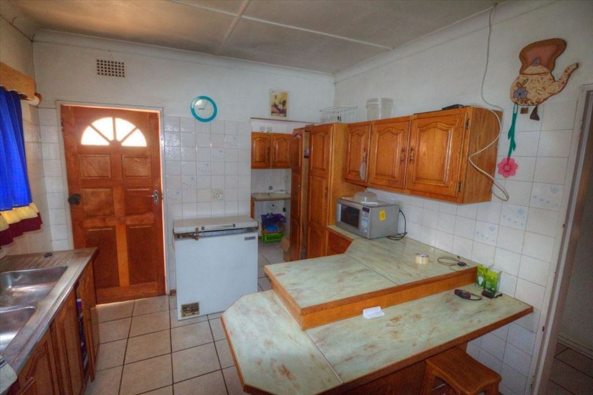 A dated kitchen featuring wooden cabinetry, laminate countertops, tiled splashbacks, and tiled flooring, providing a functional space with potential for modernization.