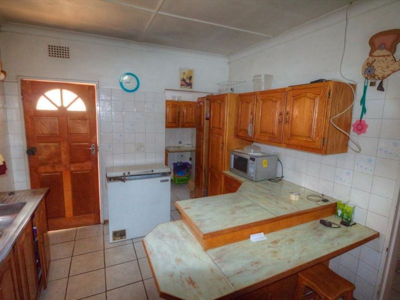 A dated kitchen featuring wooden cabinetry, laminate countertops, tiled splashbacks, and tiled flooring, providing a functional space with potential for modernization.